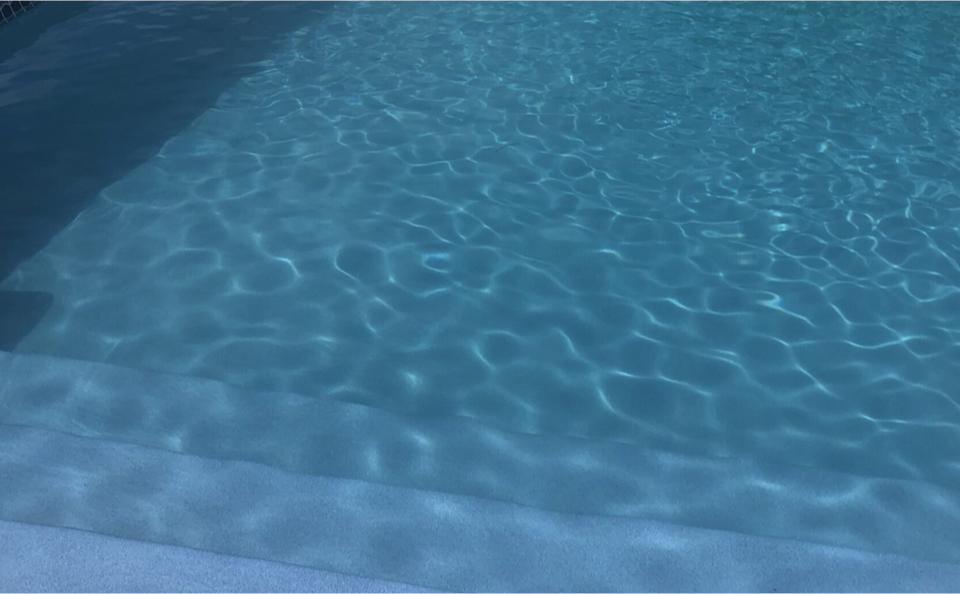Marches immergées d’une piscine au revêtement Aquabright bleu clair, visibles sous l’eau avec les reflets ondulants de la lumière.