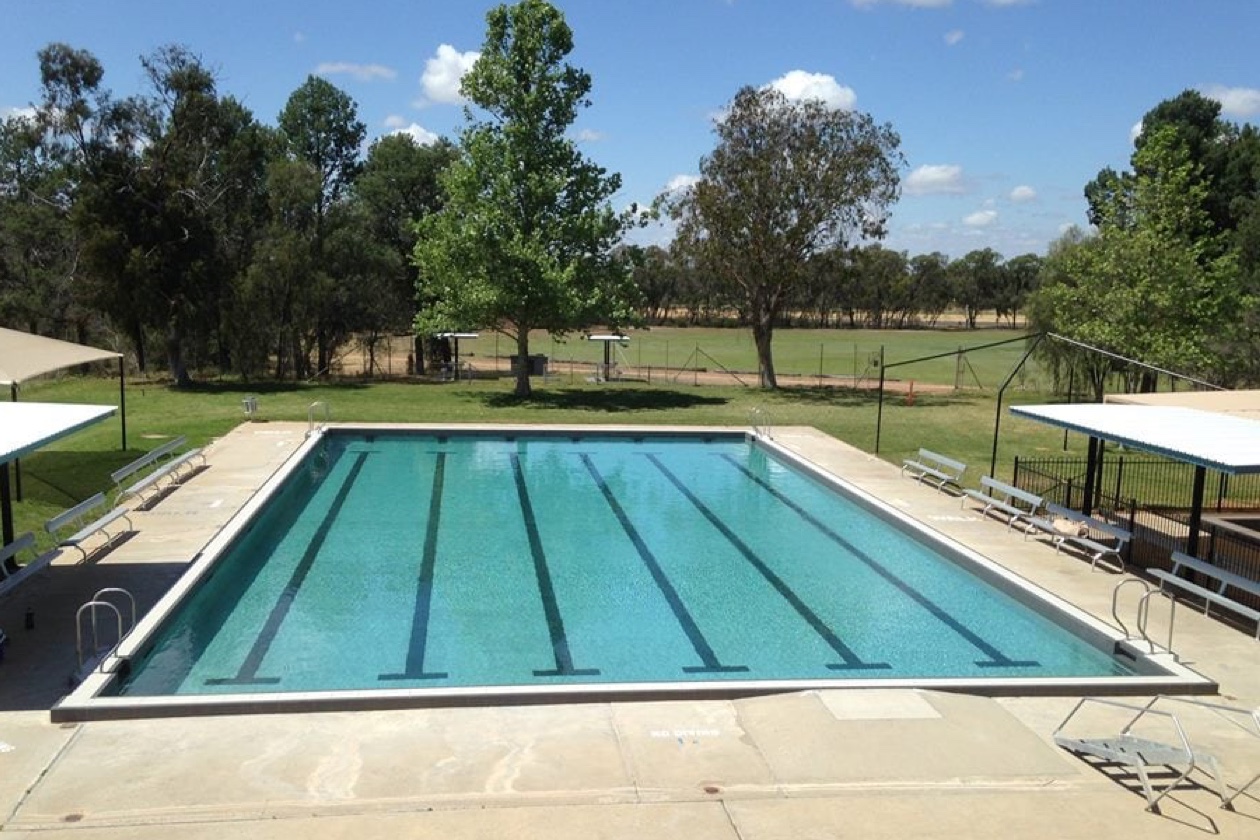 Grande piscine extérieure rectangulaire avec couloirs de nage, eau turquoise et revêtement Aquabright, entourée d’une terrasse en béton.