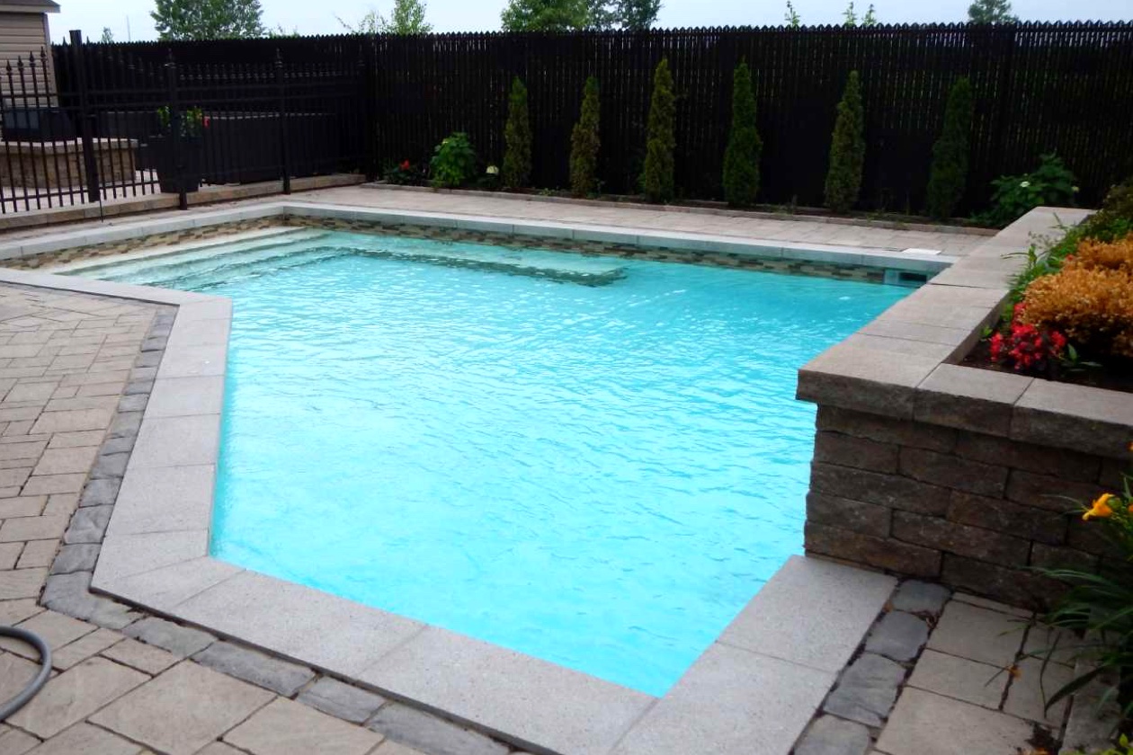 Piscine résidentielle à l’eau turquoise avec revêtement Aquabright, escalier immergé et terrasse en pavés bordée d’un aménagement fleuri.