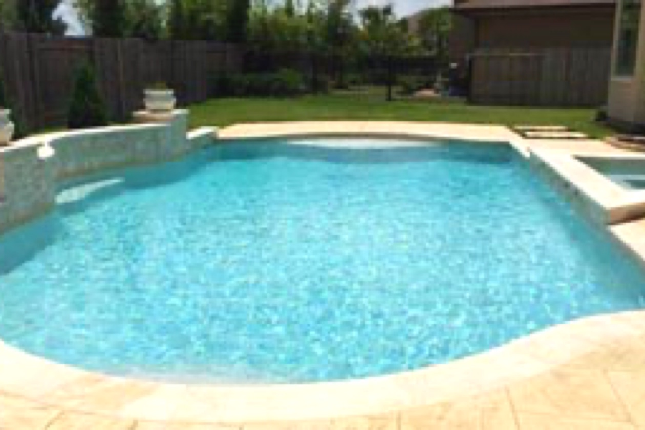 Piscine résidentielle aux formes arrondies, avec eau turquoise, revêtement Aquabright bleu clair, terrasse beige et spa adjacent.