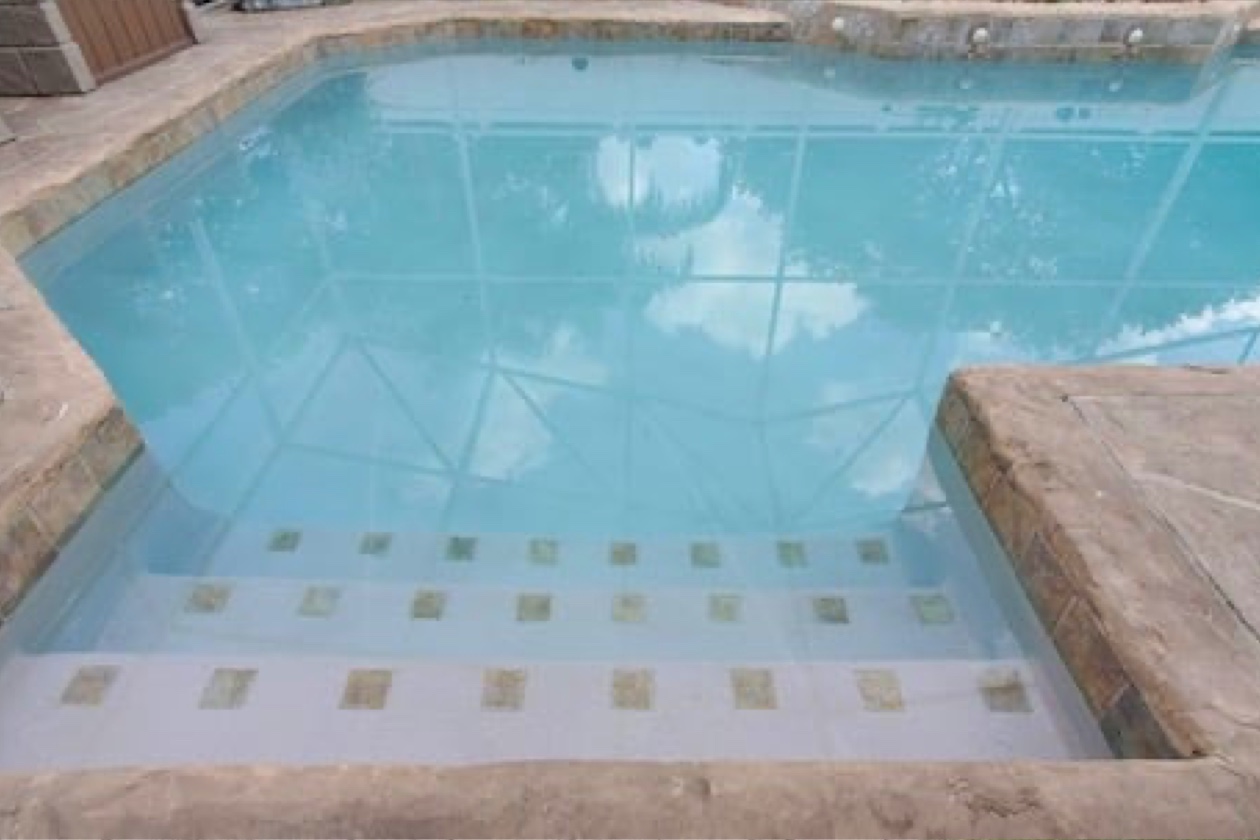 Escalier immergé orné de carreaux carrés dans une piscine au revêtement Aquabright bleu clair, entourée d’une large bordure en pierre.