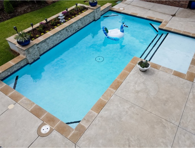 Piscine résidentielle au revêtement Aquabright bleu clair, avec plage immergée, bandes noires et bouée en forme de cygne sur l’eau.