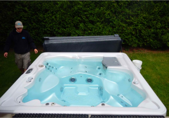 Technician beside a filled outdoor spa, ready to operate after cleaning and seasonal opening.